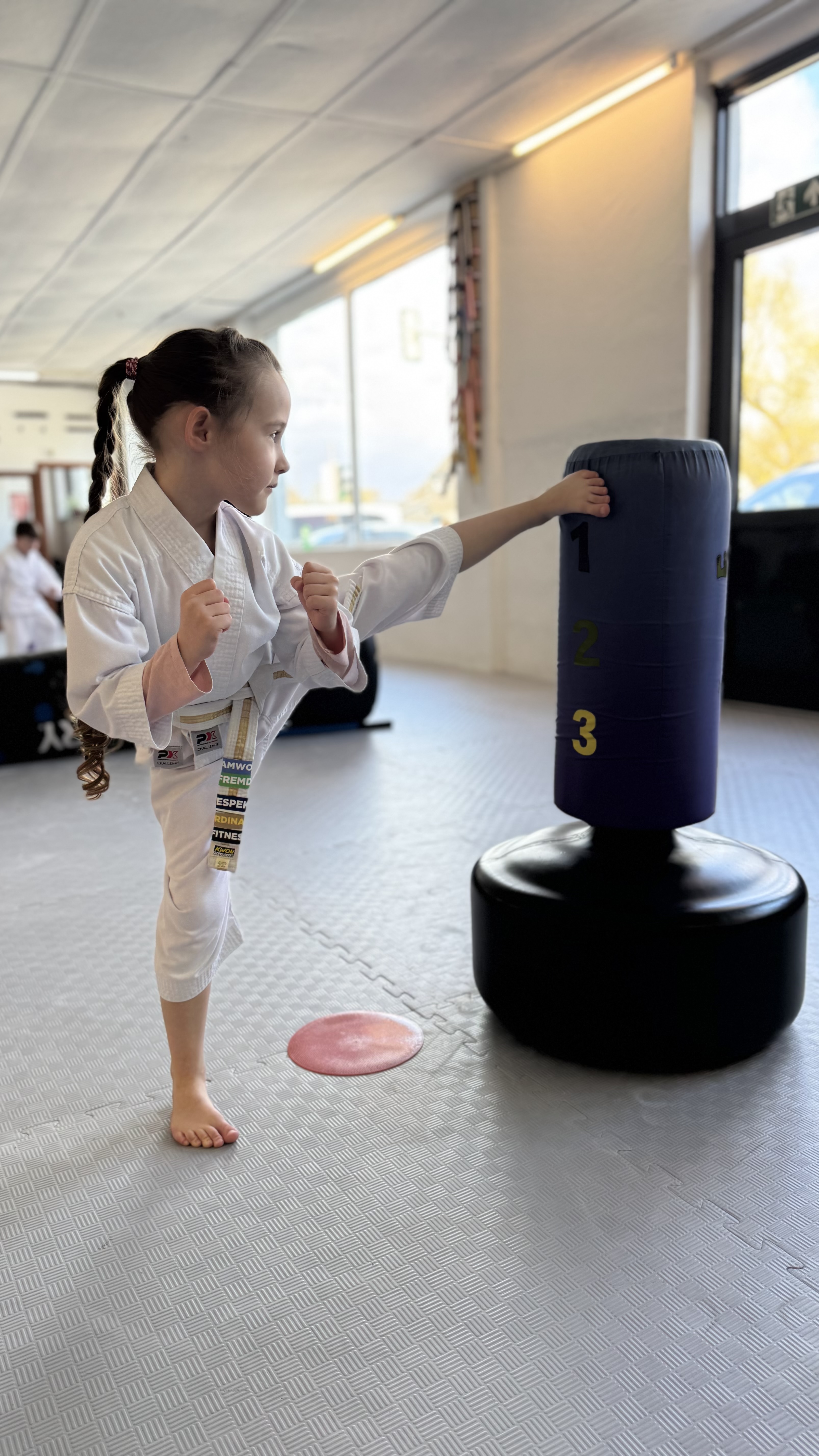 Mädchen im weißen Kampfkunstanzug tritt konzentriert gegen einen Standboxsack – INSPIRE HEROES Detmold